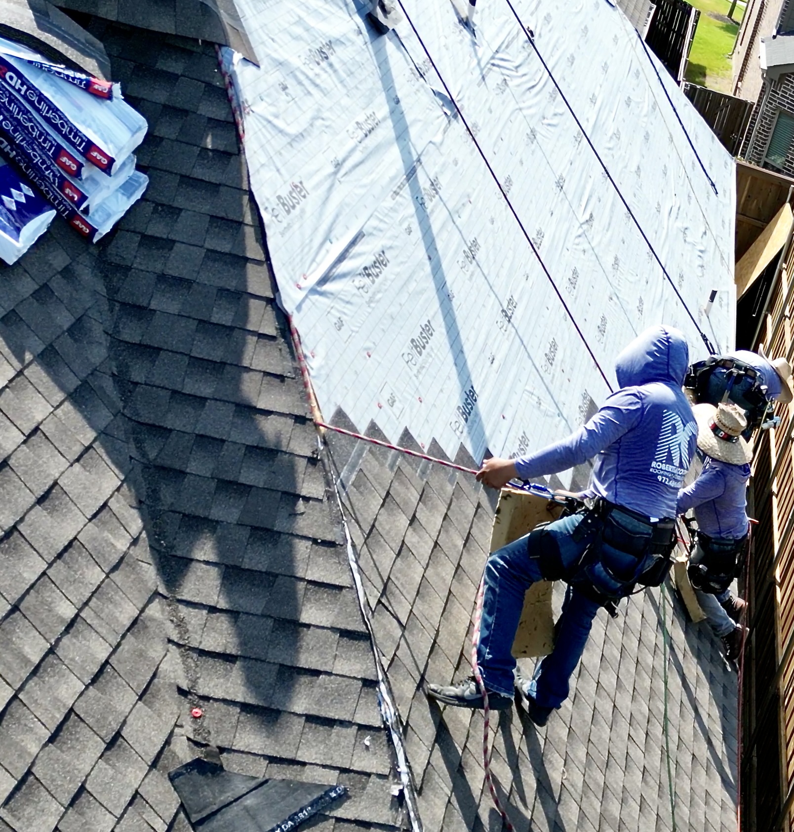Men are hanging in harnesses, installing a roof onto a home.